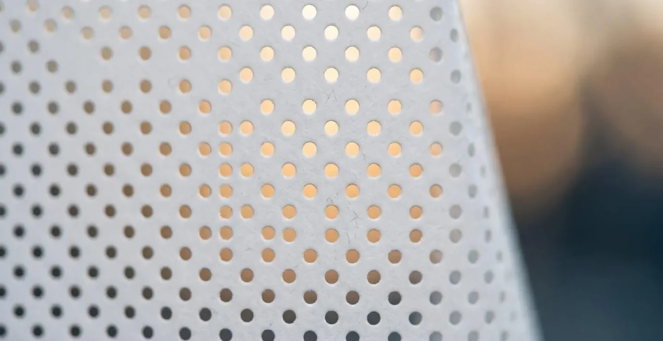 Gros plan sur la texture micro-perforée d'un adhésif de vitrine montrant les petits trous laissant passer la lumière
